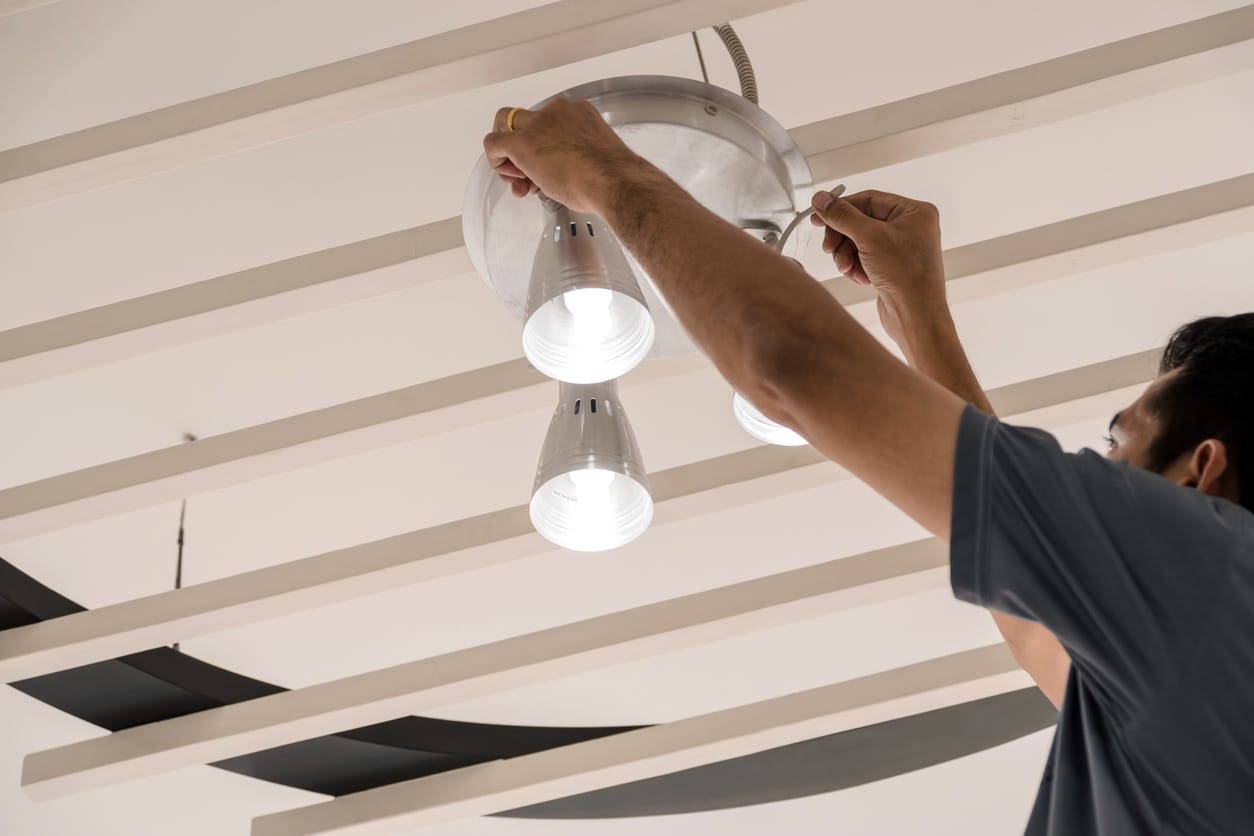 A person fixing a ceiling light fixture with three spotlights.