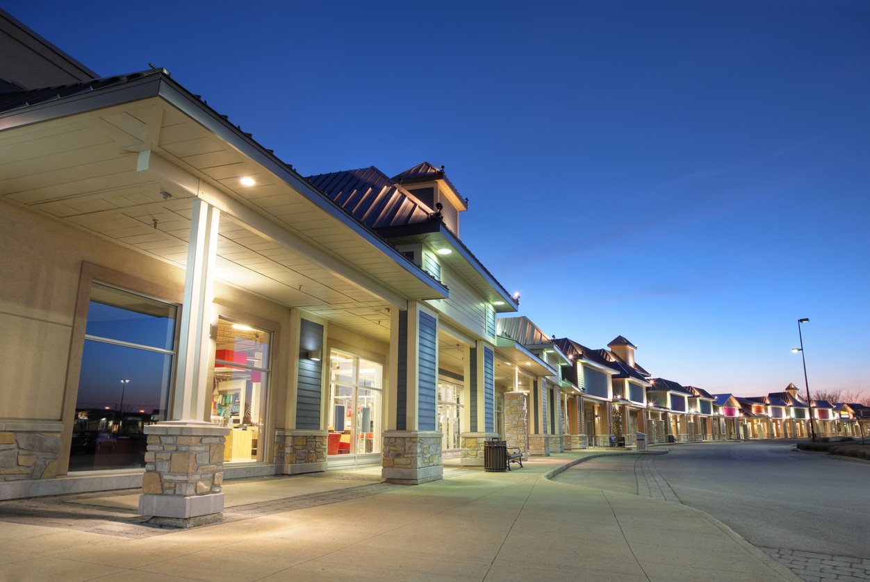 Empty shopping plaza illuminated at dusk with clear blue sky.